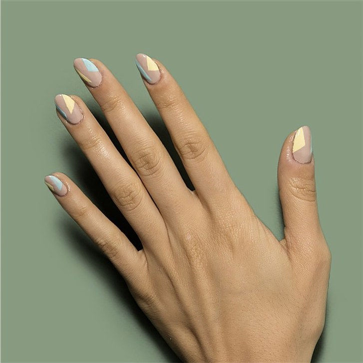 A hand with a color blocked manicure (light blue and yellow triangles on a nude base) by Chillhouse
