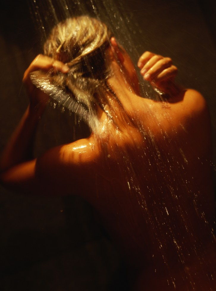Mladý woman in shower rinsing hair, rear view, close-up