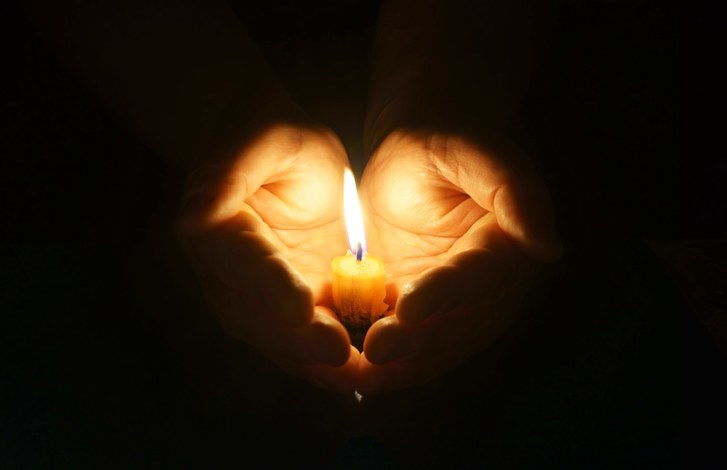 Hände, die eine brennende Kerze in der Dunkelheit anhalten. Schalenförmige Hände mit brennender Kerze. Sanfter Schutz von zerbrechlichem Feuer.