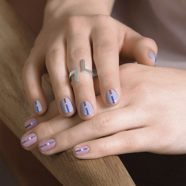 A manicure with a muticolored line and a dot in the center on a pink base on the left hand and a blue base on the right hand. Manicure by Sundays Studio.